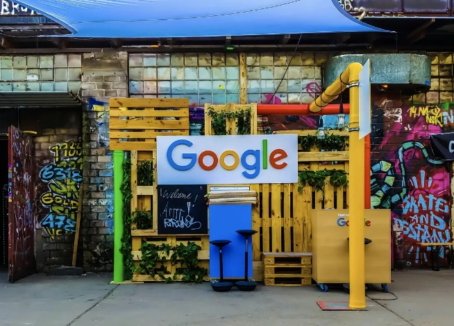 Buntes Google-Logo in einem urbanen Setting aus Holzpaletten, Pflanzen und einer Backsteinwand zum Thema Google Business.