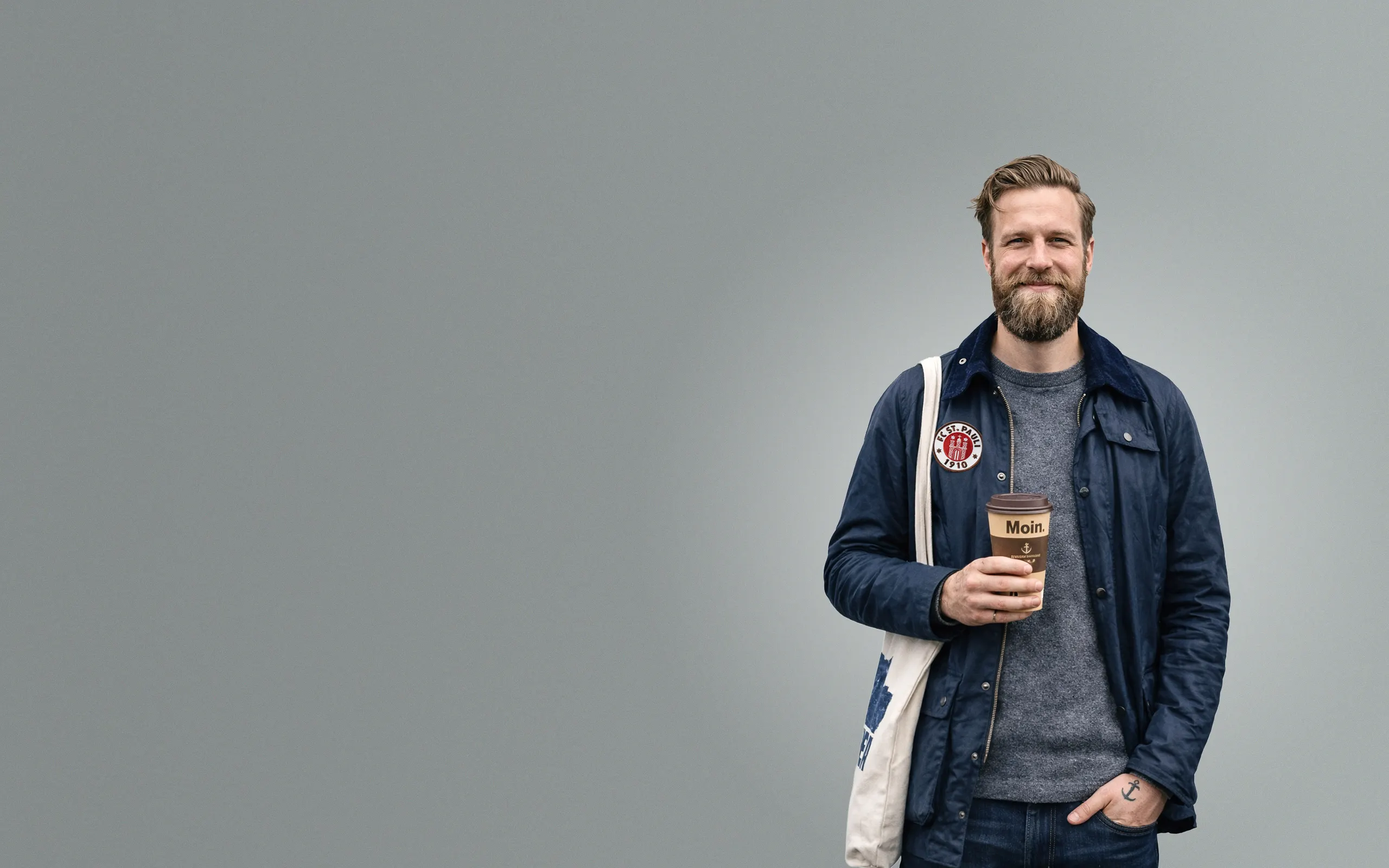 Authentischer Hamburger Kunde mit Moin-Kaffeebecher und FC St. Pauli Patch nach erfolgreicher Google Ads Kampagne.