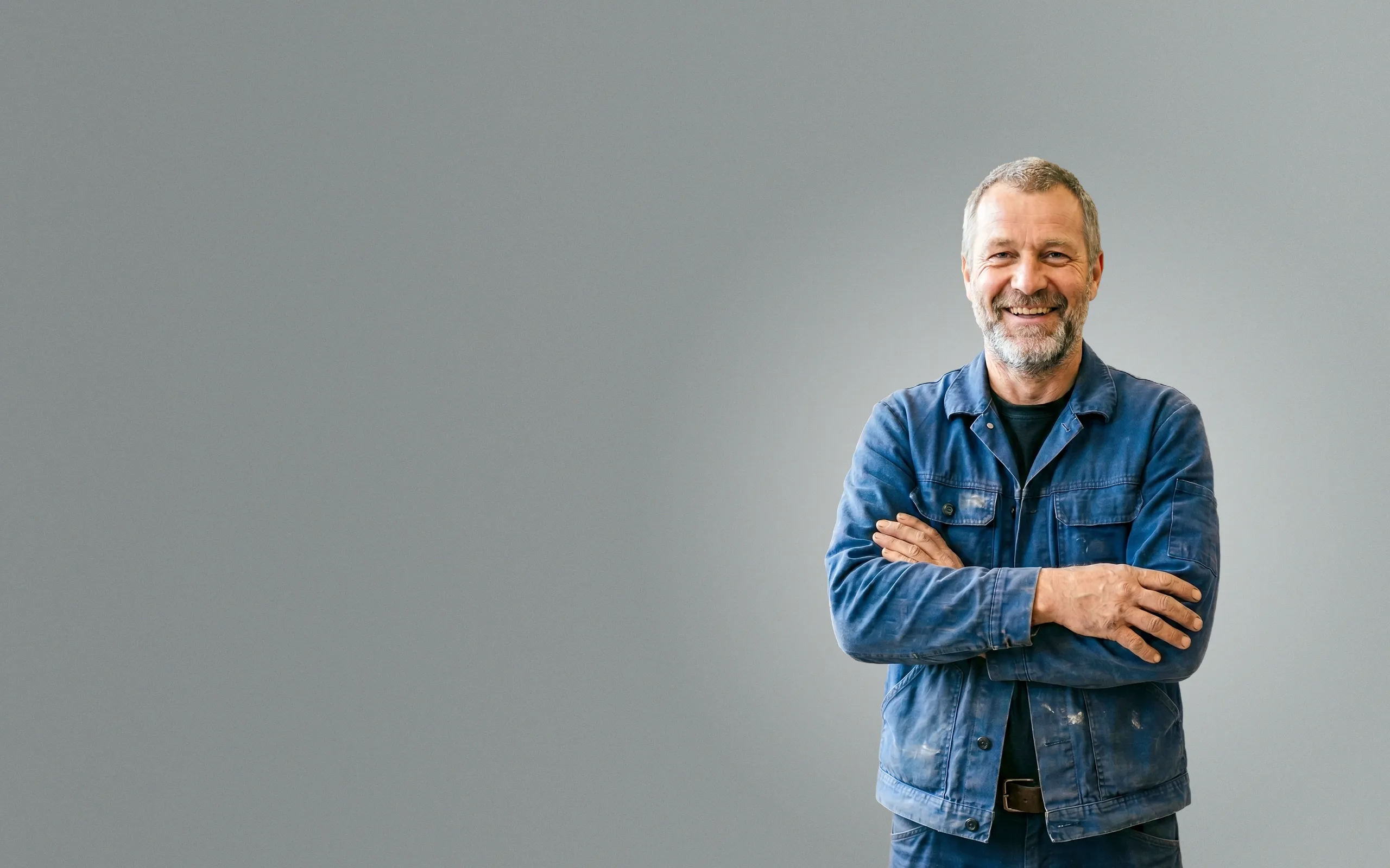 Sympathischer Handwerker in blauer Arbeitskleidung mit verschränkten Armen lächelt in die Kamera – Symbolbild für SEO, SEA und professionelles Webdesign für Handwerk und Bauunternehmen.