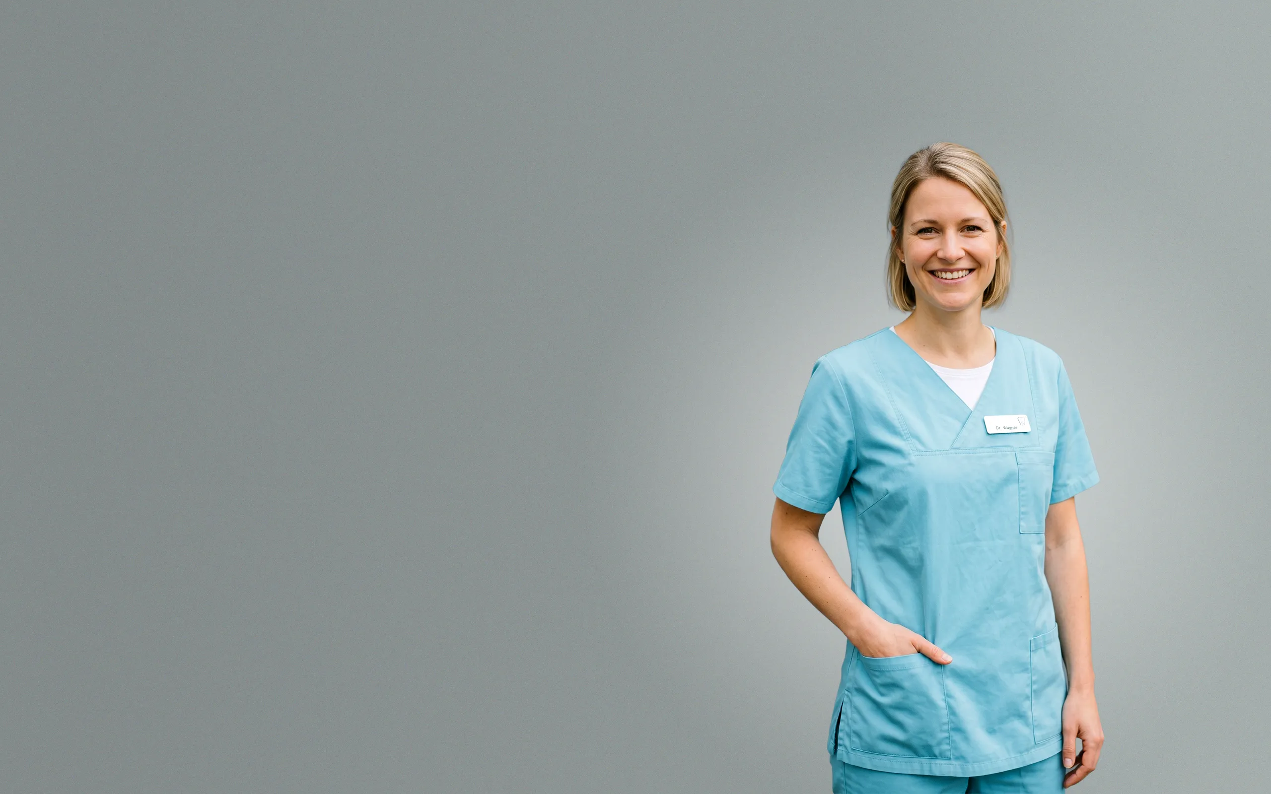 Sympathische Zahnärztin in hellblauer Praxiskleidung lächelt in die Kamera – Symbolbild für erfolgreiches Praxismarketing, SEO und Webdesign für Zahnärzte.