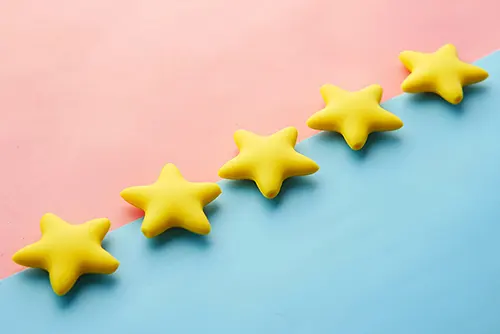 Fünf gelbe Sterne liegen diagonal auf einem zweifarbigen Hintergrund in Rosa und Blau, symbolisch für eine perfekte 5-Sterne-Kundenbewertung.