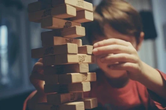 Person zieht Jenga-Stein aus einem Turm, Symbol für strategische Planung im SEO/SEA-Mix.